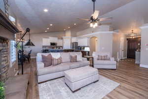 Living area featuring vaulted ceiling, light wood-style flooring, a chandelier, a ceiling fan, and arched walkways