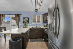 Kitchen featuring a peninsula, appliances with stainless steel finishes, dark brown cabinetry, light countertops, and light tile patterned floors