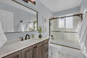 Bathroom featuring vanity, shower / bath combination with glass door, and light marble finish floors