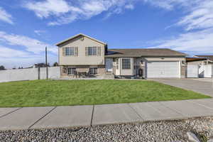 Tri-level home with an attached garage, concrete driveway, brick siding, entry steps, and a patio