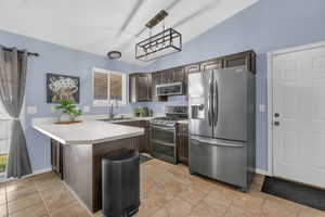 Kitchen with dark brown cabinets, light countertops, appliances with stainless steel finishes, a peninsula, and hanging light fixtures