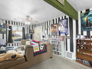 Living room with carpet flooring, a textured ceiling, ceiling fan, and wallpapered walls