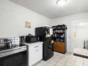 Kitchen featuring black appliances, white cabinets, light countertops, a textured ceiling, and light tile patterned flooring