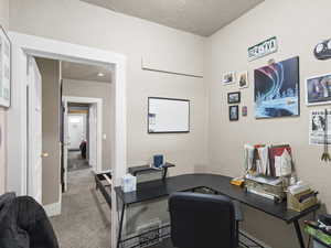 Carpeted office featuring a textured ceiling and a textured wall