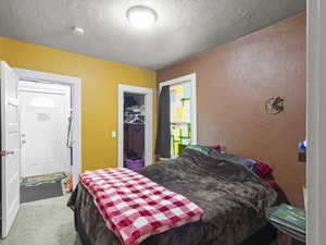 Bedroom with a textured wall, a textured ceiling, carpet floors, and a spacious closet