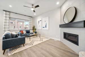 Living area with light wood-style flooring, ceiling fan, a tile fireplace, and recessed lighting
