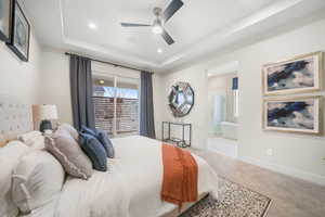 Carpeted bedroom featuring a raised ceiling, a ceiling fan, connected bathroom, and recessed lighting