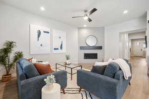 Living room with light wood-type flooring, ceiling fan, a large fireplace, and recessed lighting