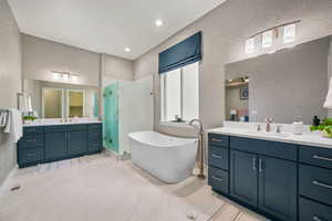 Bathroom with a stall shower, a freestanding tub, two vanities, recessed lighting, and a textured wall