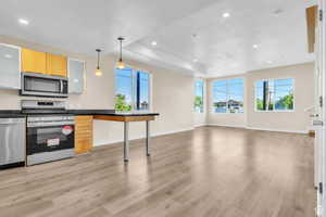 Kitchen with stainless steel appliances, hanging light fixtures, dark countertops, recessed lighting, and open floor plan