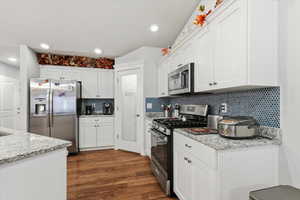 Kitchen with appliances with stainless steel finishes, light stone countertops, white cabinets, dark wood-style flooring, and recessed lighting