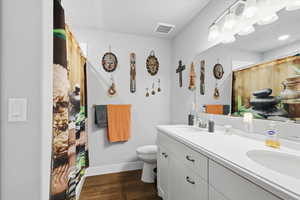 Full bath with double vanity, dark wood-style flooring, and a shower with curtain