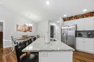 Kitchen with stainless steel fridge with ice dispenser, white cabinets, a kitchen bar, light stone countertops, and vaulted ceiling