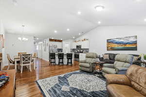 Living room featuring vaulted ceiling, recessed lighting, dark wood-style floors, and a chandelier