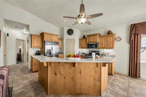 Kitchen featuring stainless steel appliances, light countertops, a kitchen bar, and a ceiling fan