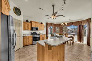 Kitchen with stainless steel appliances, a center island with sink, light tile patterned flooring, and a chandelier