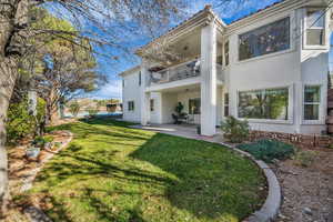Back of property with stucco siding, a balcony, a patio area, a lawn, and a tile roof