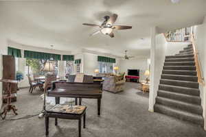 Living room with stairs, carpet, and ceiling fan
