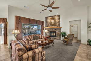 Living area with light tile patterned flooring, a stone fireplace, ceiling fan, and high vaulted ceiling