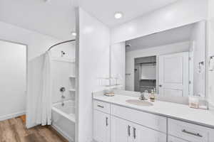 Bathroom featuring shower / bathtub combination with curtain, vanity, dark wood-style floors, and a walk in closet