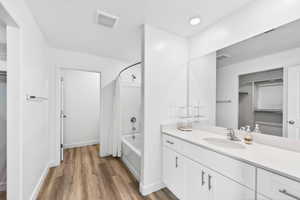 Full bathroom featuring a walk in closet, shower / bath combo with shower curtain, vanity, and dark wood-type flooring