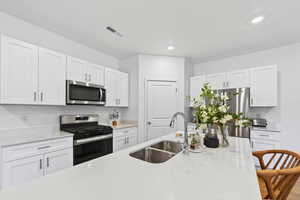 Kitchen with white cabinetry, appliances with stainless steel finishes, light stone countertops, and recessed lighting