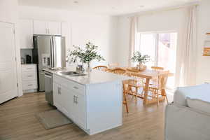 Kitchen featuring white cabinets, light wood finished floors, light stone countertops, a kitchen island with sink, and stainless steel appliances