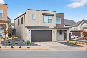 Contemporary house featuring stone siding, stucco siding, a garage, and driveway