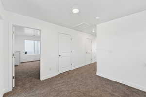 Unfurnished bedroom featuring dark colored carpet and attic access