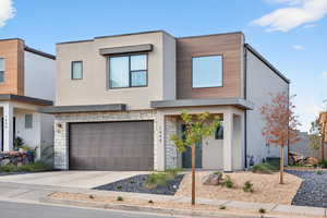 Modern home with stucco siding, an attached garage, stone siding, and driveway