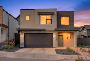 Contemporary house featuring stone siding, stucco siding, a garage, and concrete driveway