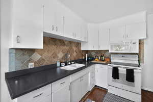 Kitchen with dark countertops, white appliances, tasteful backsplash, white cabinets, and dark wood finished floors