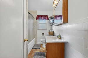 Full bathroom featuring vanity, combined bath / shower with glass door, and tile walls
