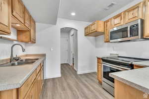 Kitchen with appliances with stainless steel finishes, arched walkways, light countertops, a textured ceiling, and light wood-style floors