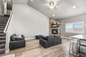 Living area with stairs, lofted ceiling, a fireplace, light wood-style flooring, and recessed lighting