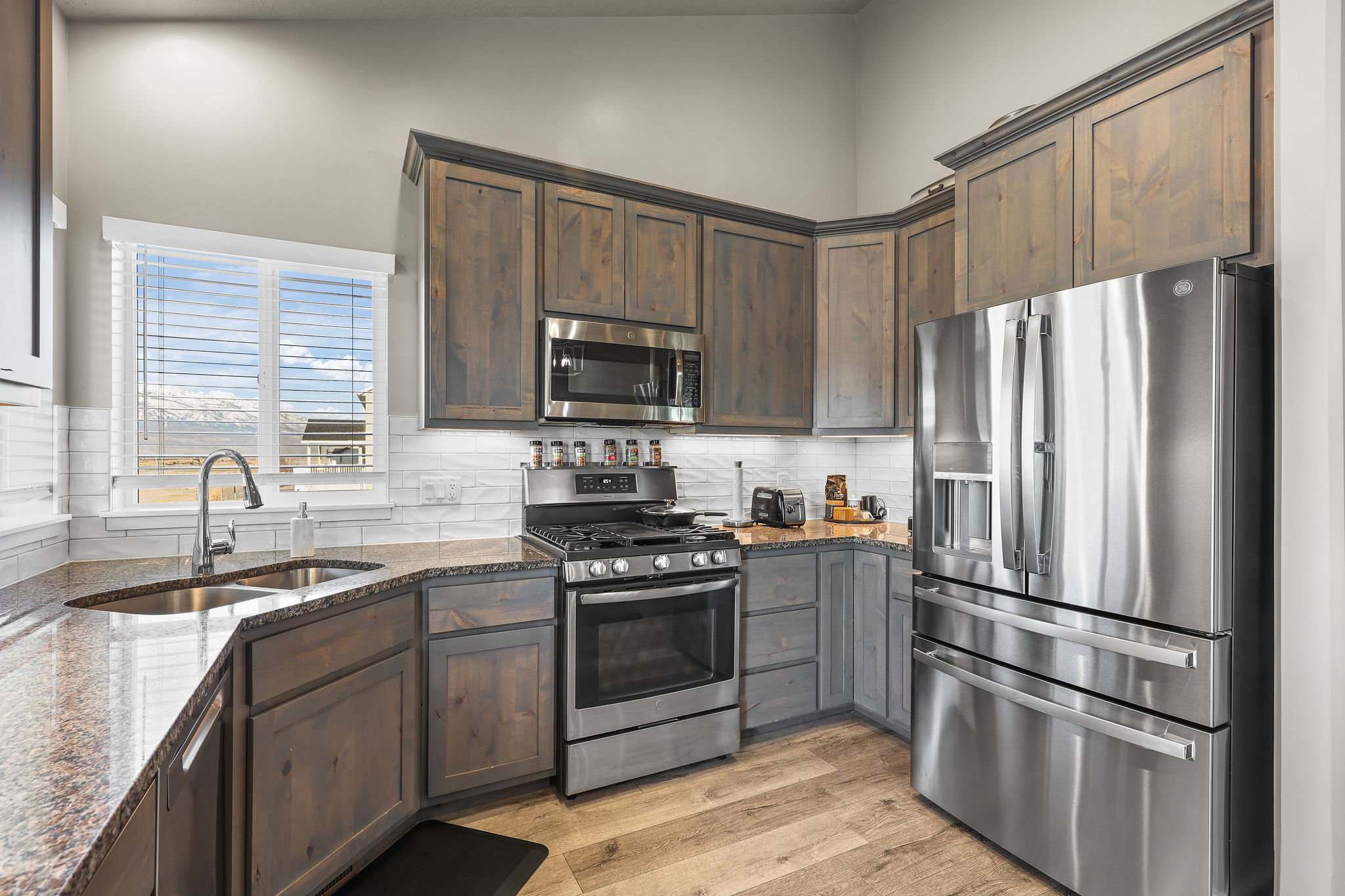Kitchen with stainless steel appliances, dark stone countertops, dark brown cabinetry, vaulted ceiling, and light wood-style flooring