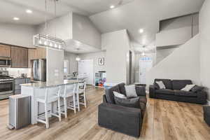 Kitchen featuring a kitchen bar, light stone countertops, appliances with stainless steel finishes, high vaulted ceiling, and open floor plan