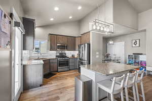 Kitchen with light stone counters, stainless steel appliances, a kitchen breakfast bar, light wood finished floors, and pendant lighting
