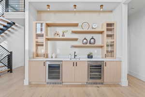 Indoor wet bar with light brown cabinetry, stairs, beverage cooler, and light stone countertops