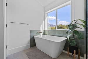 Bathroom featuring tile walls, a freestanding tub, a mountain view, and light tile patterned flooring