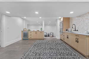 Bar area with light brown cabinets, wine cooler, recessed lighting, stainless steel double oven, and an accent wall