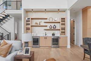 Indoor wet bar featuring light brown cabinets, stairway, beverage cooler, and light wood-style flooring