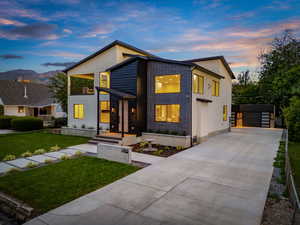 Contemporary house featuring concrete driveway, a front lawn, stucco siding, and a balcony