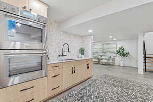 Kitchen with light brown cabinets, double oven, recessed lighting, light stone countertops, and light wood-style floors