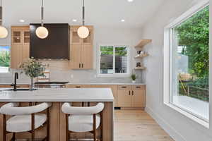 Kitchen featuring light brown cabinets, light stone countertops, pendant lighting, open shelves, and a kitchen bar