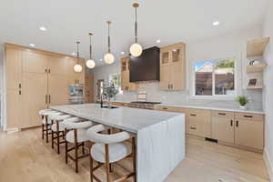Kitchen featuring light brown cabinets, a kitchen bar, light stone countertops, healthy amount of natural light, and recessed lighting