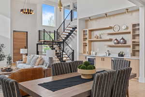 Dining room featuring light wood finished floors, stairway, bar with sink, beverage cooler, and a towering ceiling