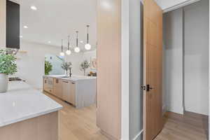Kitchen featuring light brown cabinets, modern cabinets, light stone countertops, decorative light fixtures, and light wood-style flooring