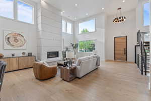 Living room featuring a high ceiling, light wood-style floors, a large fireplace, and recessed lighting