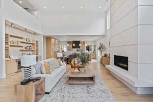 Living room featuring a towering ceiling, a glass covered fireplace, light wood-style flooring, recessed lighting, and beverage cooler